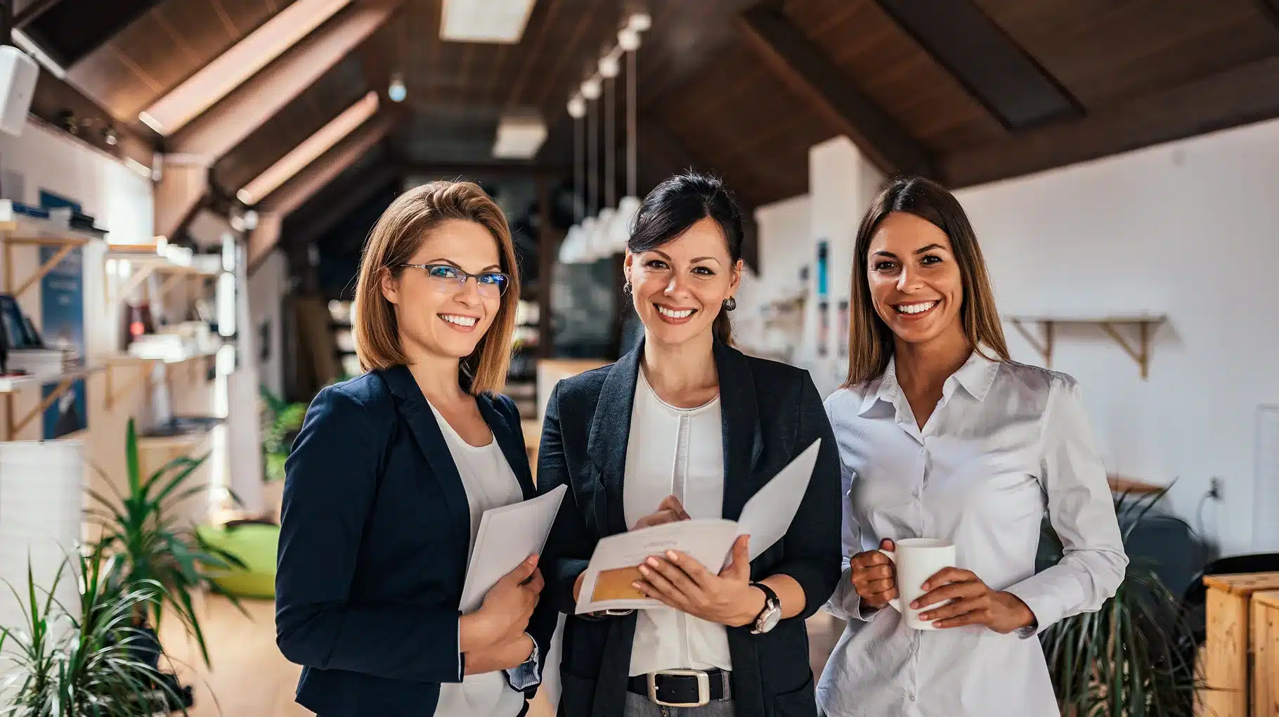 Three businesswomen standing together in a modern office, engaged in conversation and collaboration.